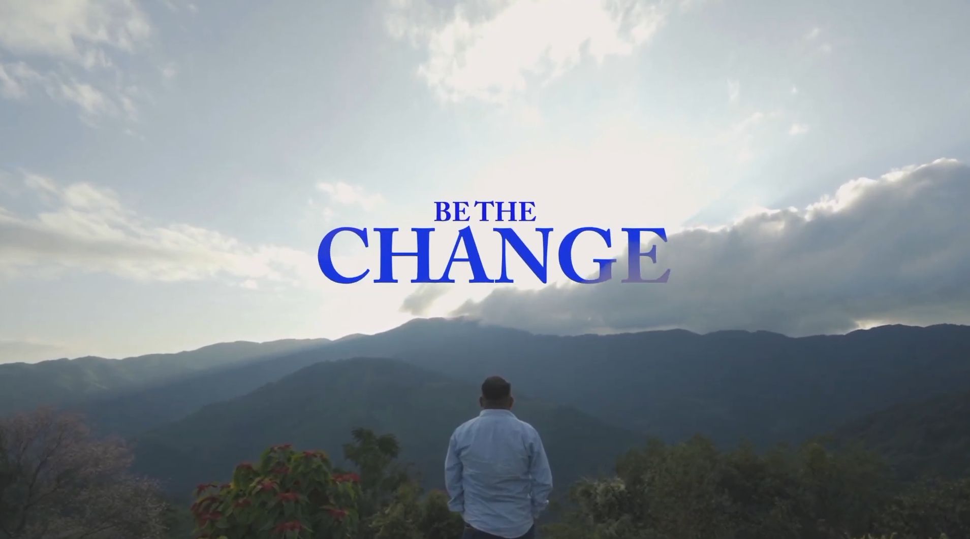 Title card reading “Be The Change” over a man standing with his back to camera, looking out across forested hill ranges in Nagaland under a wide cloudy sky.